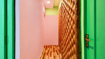 A hallway with a wooden floor, a pink wall, and a green door.
