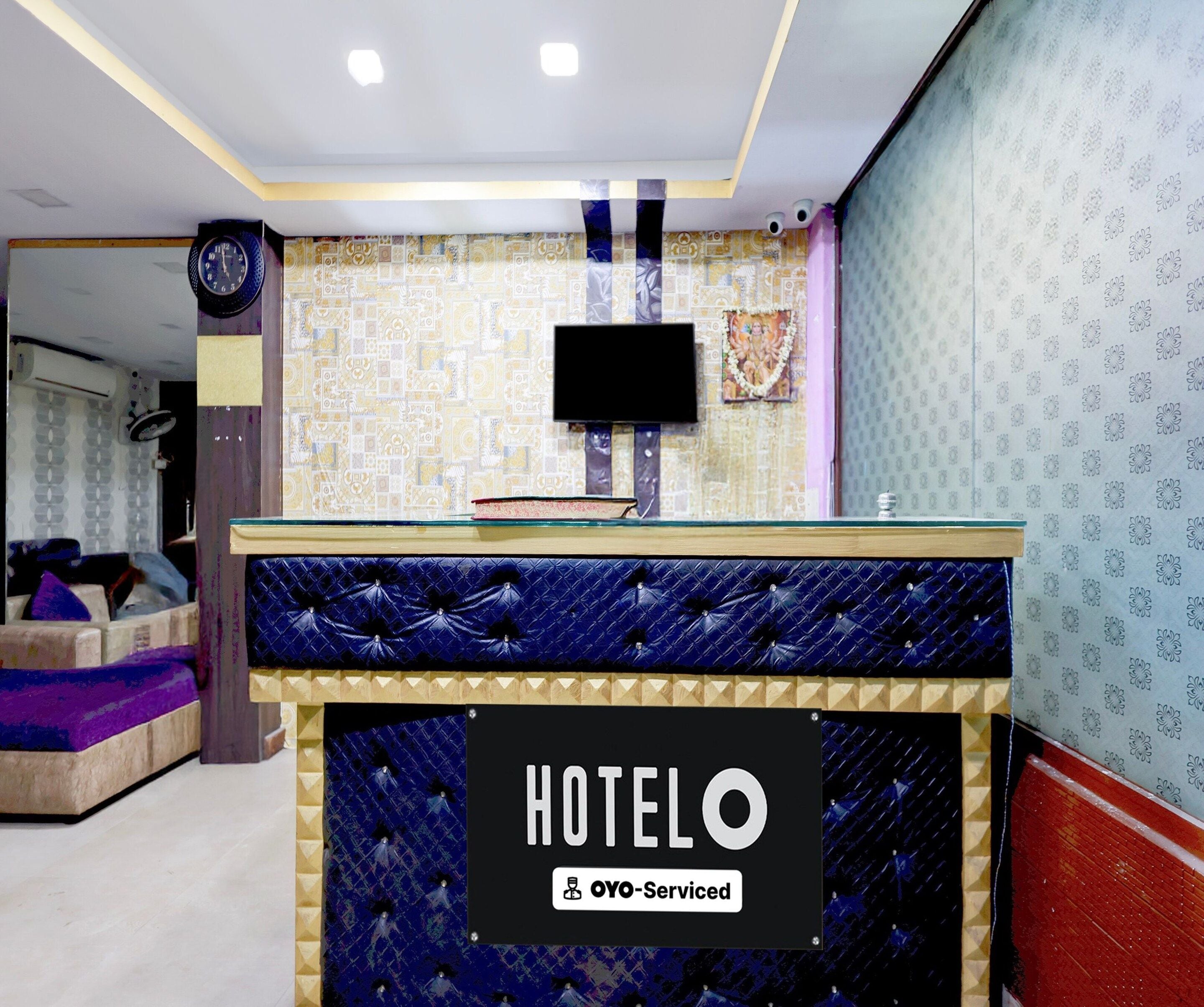 A hotel reception area with a blue cushioned seating area, a reception desk, and a television mounted on the wall.