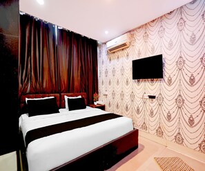 A hotel room with a large bed, dark curtains, a wall-mounted TV, and a patterned wallpaper. - Saver Double Royal Inn Guest House (Kolkata)
