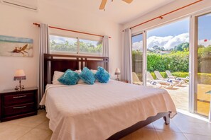 Un dormitorio con una cama grande, una mesita de noche, una lámpara y vistas a un jardín a través de un ventanal corredizo.