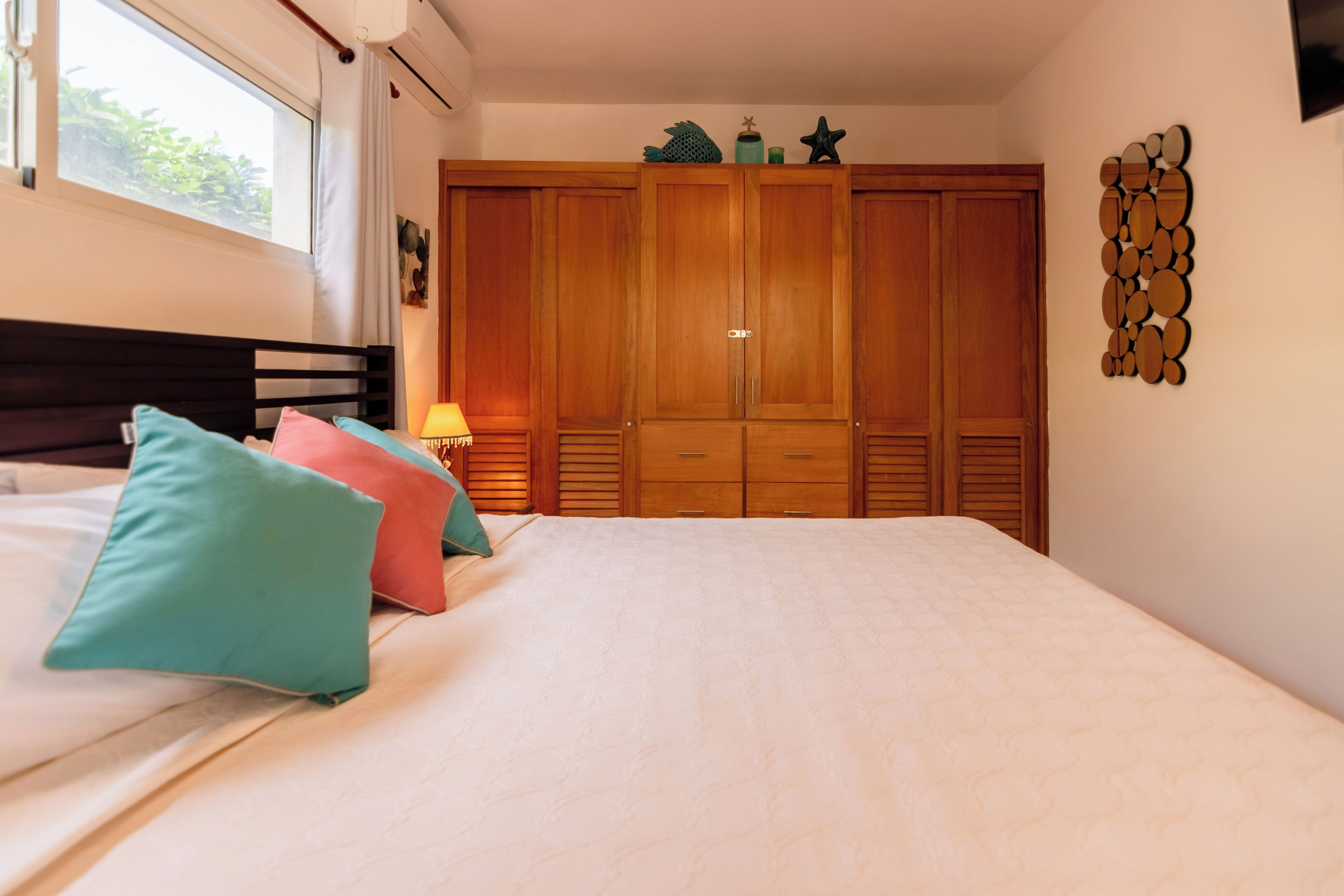 Un dormitorio con cama, almohadas, una mesita de noche, un armario y un adorno en la pared.