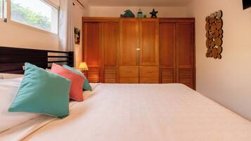 Un dormitorio con cama, almohadas, una mesita de noche, un armario y un adorno en la pared.