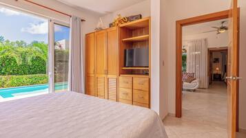 A bedroom with a large bed, wooden wardrobe, and a TV. There's a sliding glass door leading to a pool.