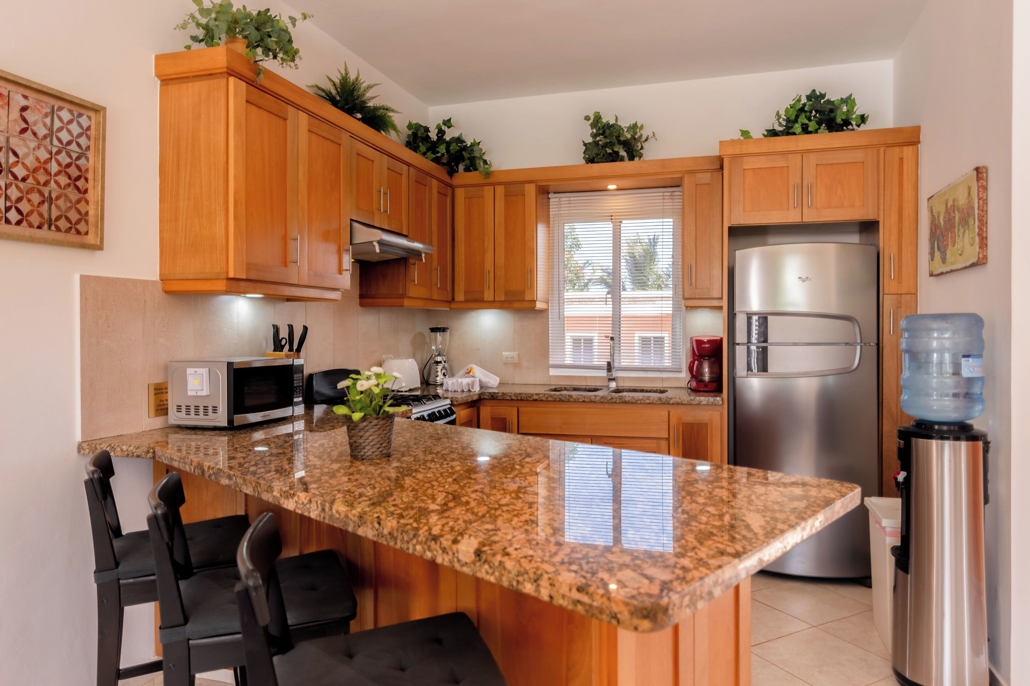 A kitchen with wooden cabinets, a granite countertop, a stainless steel refrigerator, and a water dispenser.