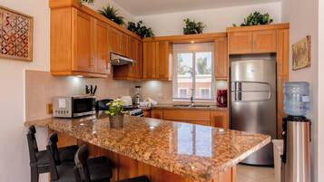 A kitchen with wooden cabinets, a granite countertop, a stainless steel refrigerator, and a water dispenser.