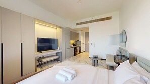 A hotel room with a bed, a TV, a small kitchen area, and a seating area with a table and chairs. - Serene Meydan Studio | Distant Burj Khalifa View (Meydan)