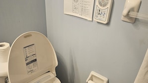 A bathroom with a toilet, a bidet, a paper towel dispenser, and a wall-mounted control panel. - Cosy Room with exclusive bathroom (Mississauga)