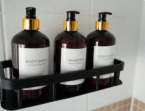 Trois bouteilles de gel douche, de shampoing et d’après-shampoing sur une étagère noire.
