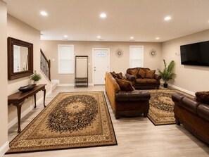Una sala de estar con un tapete grande estampado, sofás de cuero, un televisor y una puerta con ventana.