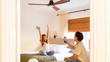 Un dormitorio con dos camas, ventilador de techo y ventana con cortinas.