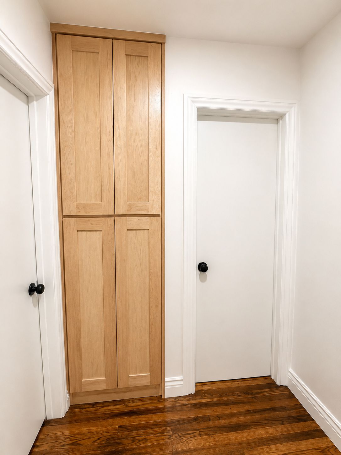 Un couloir doté d’un plancher en bois et de murs blancs, avec une porte double et une porte simple.