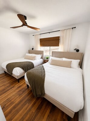 Ein Schlafzimmer mit zwei Betten, einem Deckenventilator, einem Fenster mit Vorhängen und einem Holzboden.