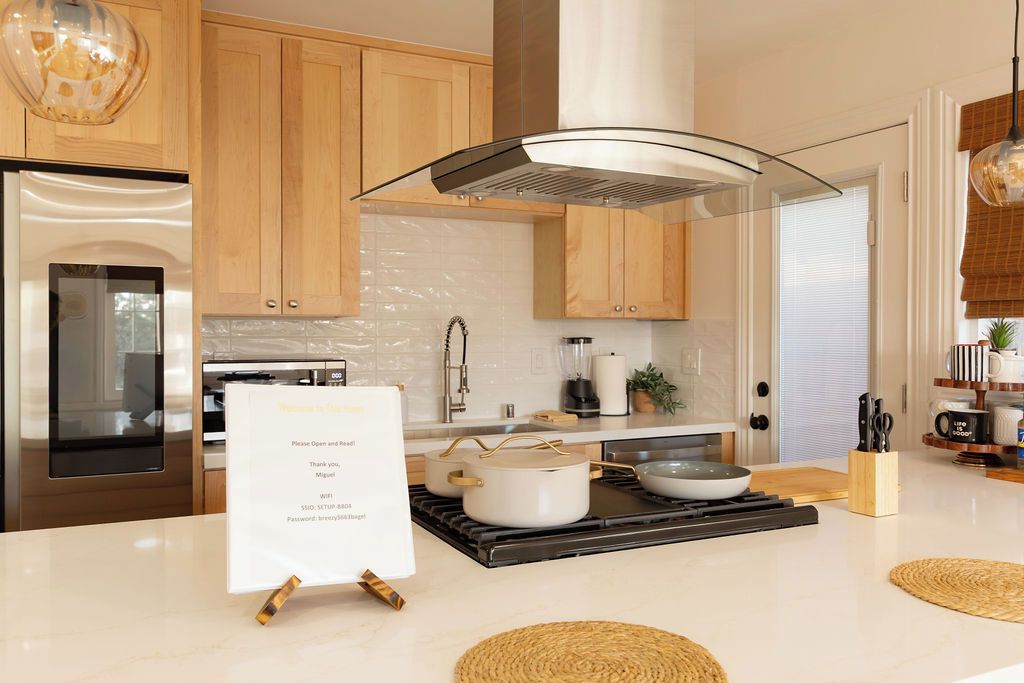 A modern kitchen with wooden cabinets, a stainless steel range, a built-in oven, a central island with a pot and a bowl, and a hanging light fixture.