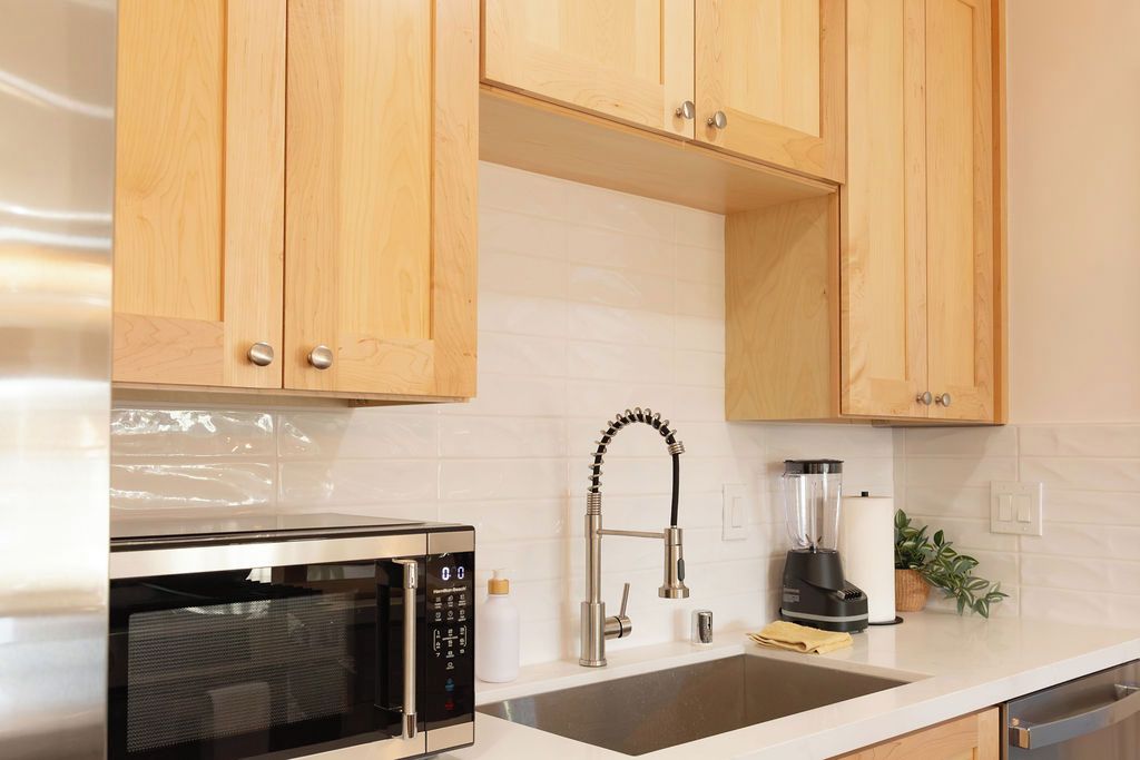 A kitchen with wooden cabinets, a stainless steel microwave, a sink, a faucet, and a blender.