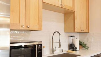 A kitchen with wooden cabinets, a stainless steel microwave, a sink, a faucet, and a blender.