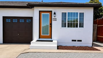 Una casa de una planta con una puerta de garaje marrón, una puerta principal blanca con panel de vidrio y una ventana pequeña.