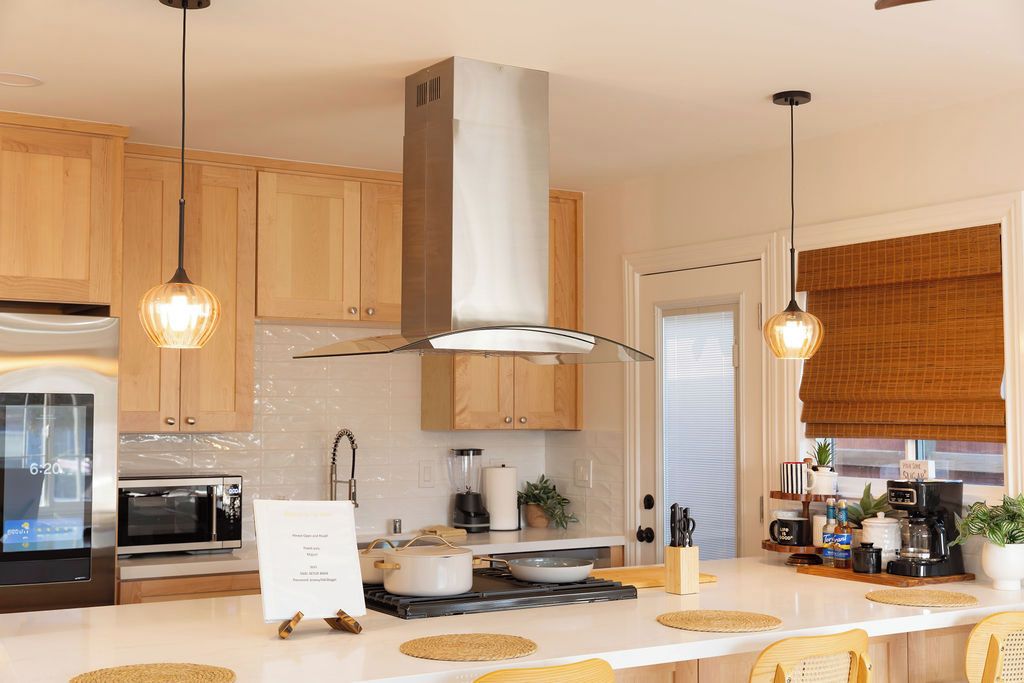 Una cocina moderna con gabinetes de madera, una campana extractora de acero inoxidable, un microondas, una estufa y una estación para café.