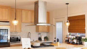 Una cocina moderna con gabinetes de madera, una campana extractora de acero inoxidable, un microondas, una estufa y una estación para café.
