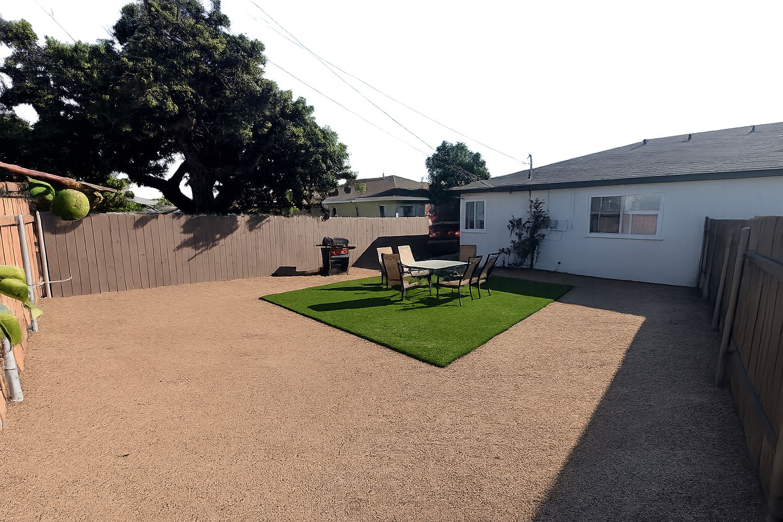 Un patio trasero con zona de patio, una parrilla y un jardín cercado.