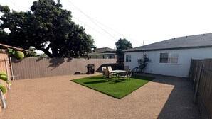 Un patio trasero con zona de patio, una parrilla y un jardín cercado.