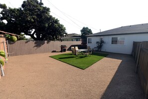Ein Garten mit einer Terrassenfläche, einem Grill und einem umzäunten Bereich.