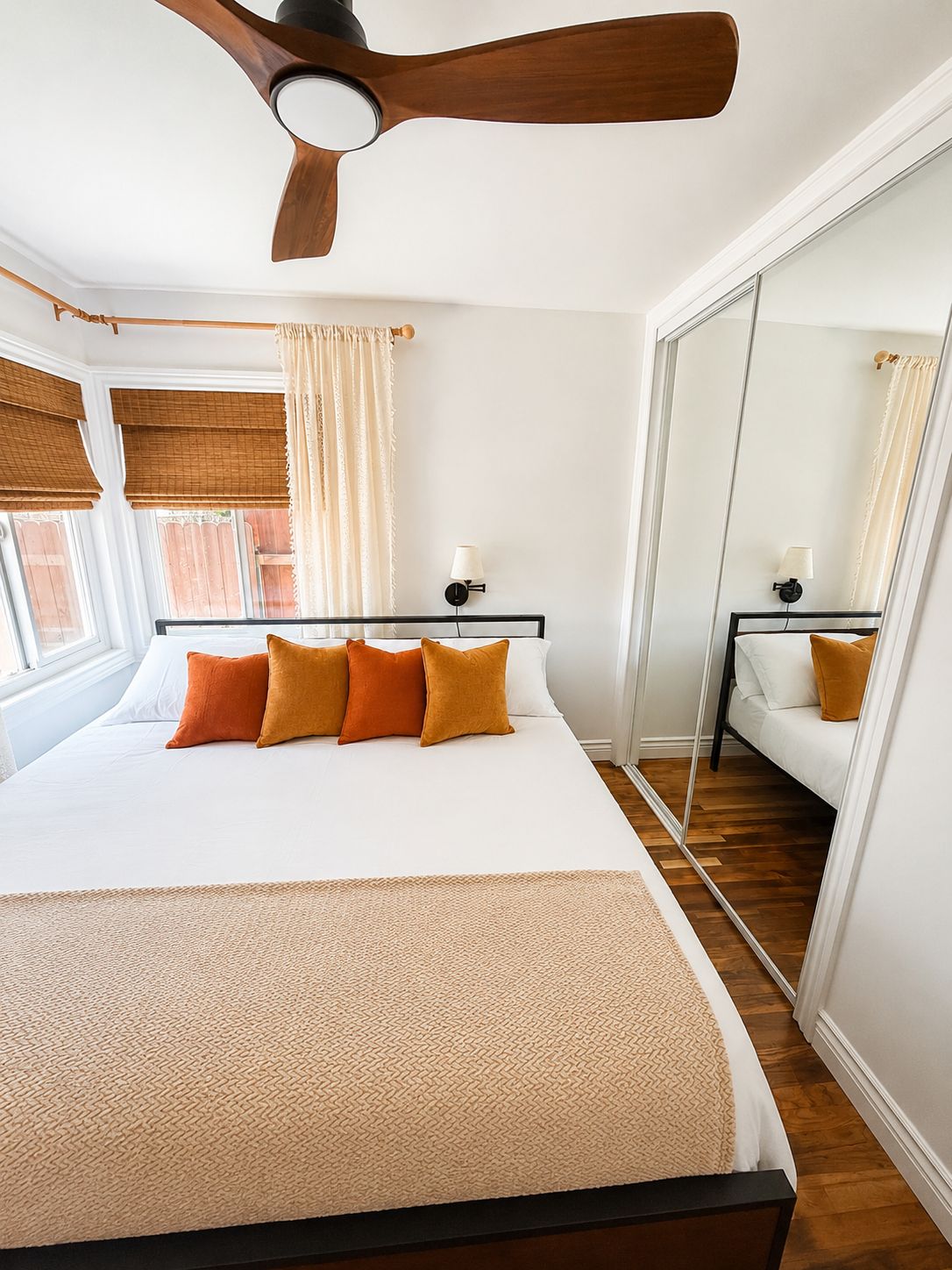Ein Schlafzimmer mit einem Bett, einem Deckenventilator, einem Nachttisch mit Lampe und einem großen Spiegel.