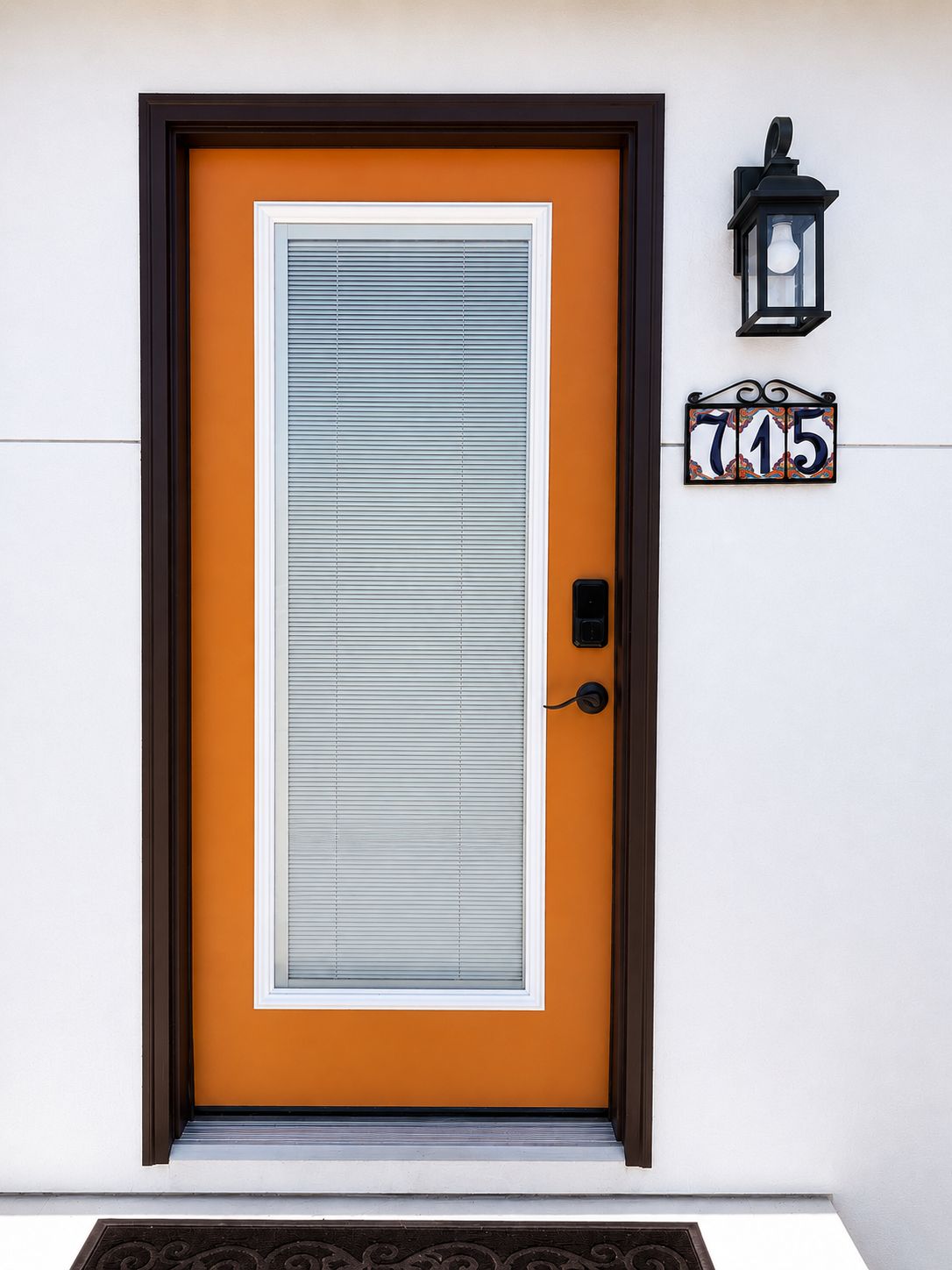Une porte avec une plaque portant un numéro, un interphone et un luminaire fixé au mur.