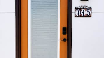 Une porte avec une plaque portant un numéro, un interphone et un luminaire fixé au mur.