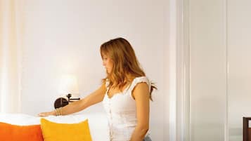 A woman adjusting a bed with white and orange pillows in a room with a white wall and a sliding door.