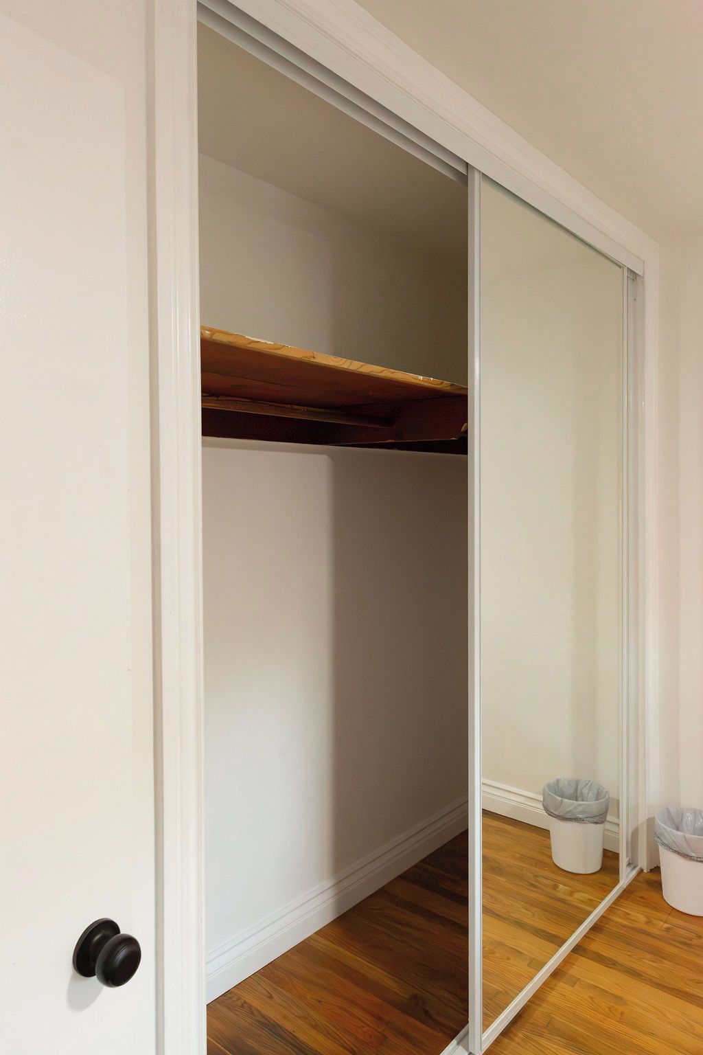 Una habitación con armario correderas, piso de madera y un pequeño cubo de basura.