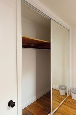 A room with a sliding door closet, wooden flooring, and a small trash bin. - Sleeps 8 • King Suite • 2 Queens (Chula Vista)