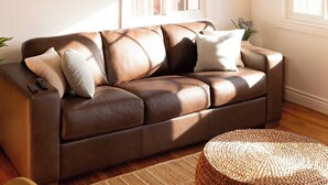 Sala de estar com sofá de couro marrom, ventilador de teto e janela com cortina marrom.