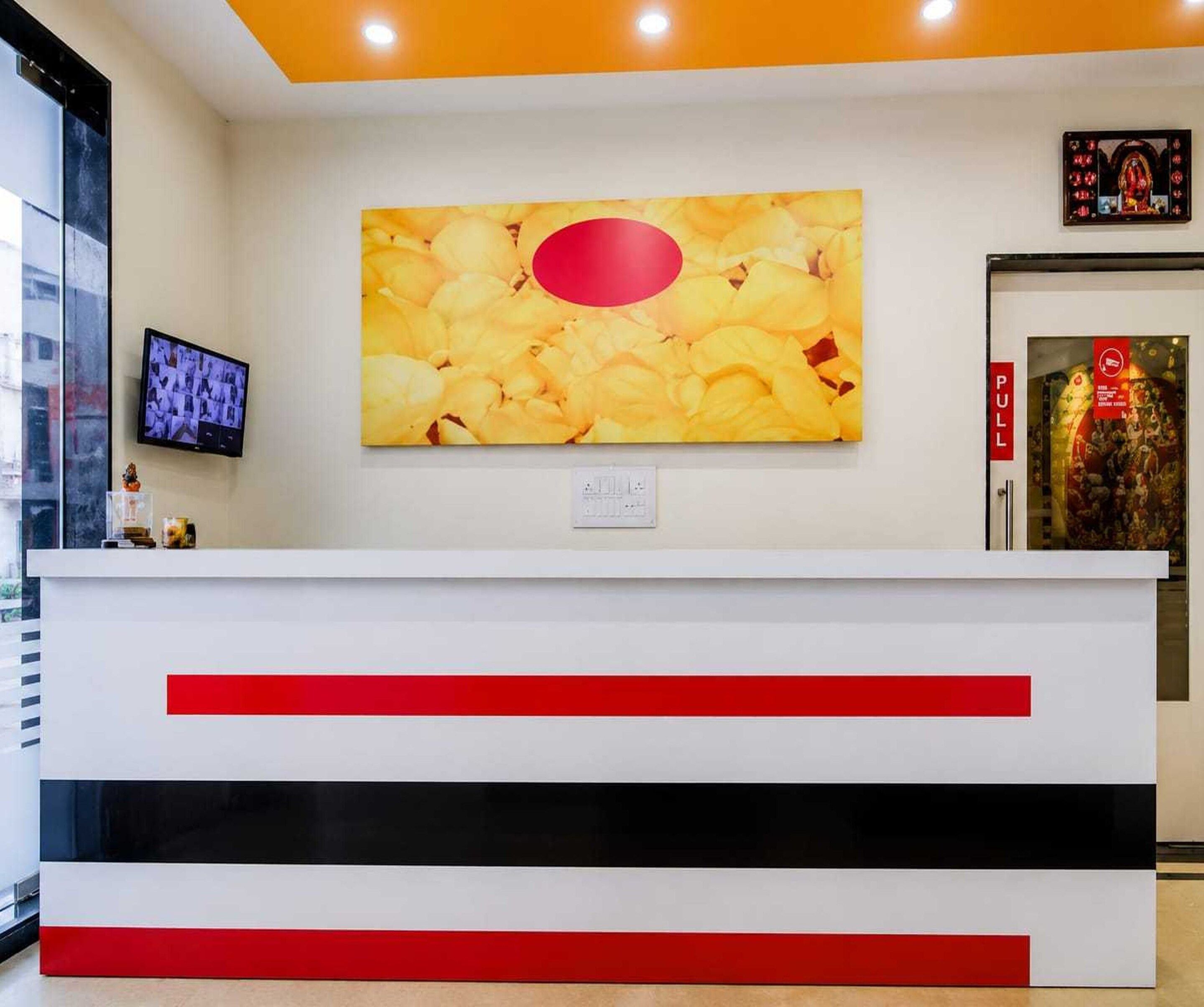 Una reception con un grande quadro sopra, uno schermo televisivo a sinistra e una porta con un cartello rosso a destra.