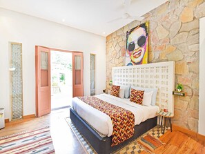 A bedroom with a stone wall, a bed with patterned bedding, a calendar, and a small table with a plant.