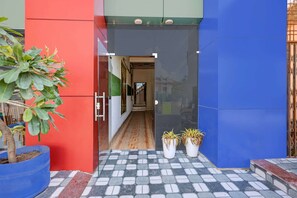 Ein Gebäudeeingang mit einer roten und blauen Fassade, einem gefliesten Weg und Blumentöpfen.
