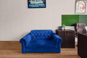 Ein Zimmer mit einem blauen Sofa, einem braunen Ledersessel, einer grünen Wand und einem gerahmten Bild.