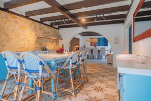 A dining area with a stone wall, a wooden ceiling, and a blue and white patterned tablecloth. - OceanView Villa Steps from Beach| Bougainvillea (Noord)