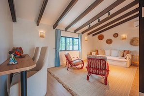Ein Zimmer mit einem Holztisch, zwei Stühlen, einem Sofa und einem Fenster mit Vorhängen.