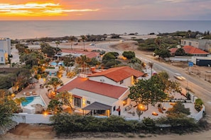 A coastal residential area with houses, a swimming pool, and a road leading to the beach. - OceanView Villa Steps from Beach| Bougainvillea (Noord)