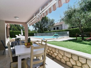 Un área de patio al aire libre con piscina, muro de piedra y mesa con sillas.