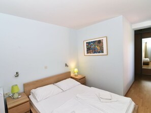 Habitación de hotel con una cama individual, mesita de noche con lámpara, enchufe y una obra de arte colgada en la pared.