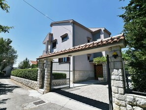 Edificio residencial de dos pisos con una entrada de piedra, techo de tejas y camino de acceso pavimentado.