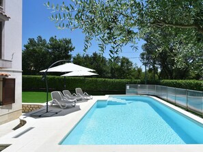Una piscina con sillas de descanso y sombrillas, rodeada de setos y árboles.