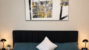 Una cama con una colcha color turquesa, un almohadón blanco en zigzag y un cabecero negro.
