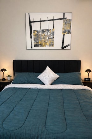 A bed with a teal comforter, a white zigzag pillow, and a black headboard. - DT Corporate Condo NR Farmers Market w/ Gym Pool (Dallas)