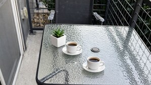 Una mesa con cubierta de vidrio, dos tazas blancas de café y una pequeña planta en maceta en un balcón.