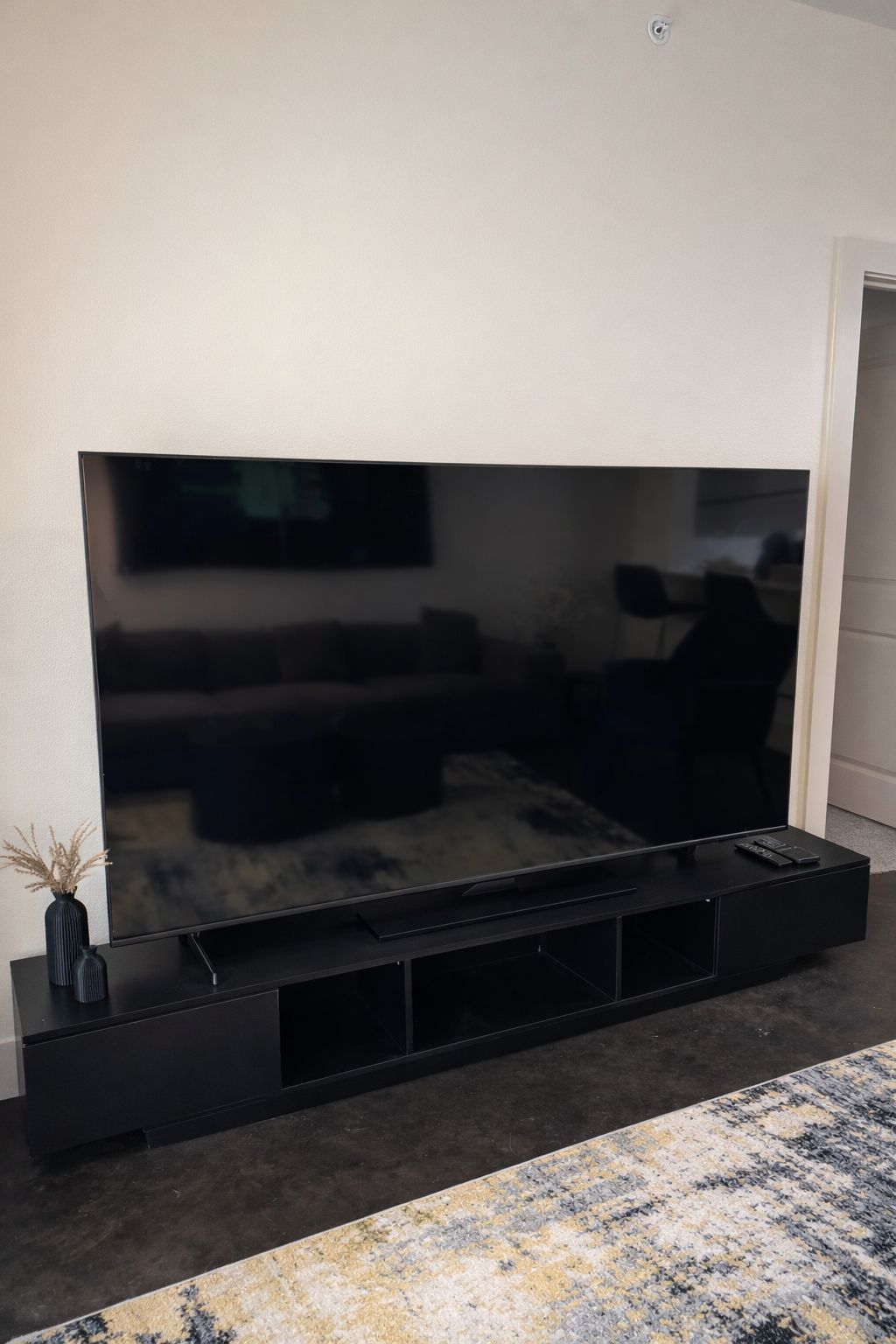 A flat-screen TV mounted on a black stand with a remote control on top.