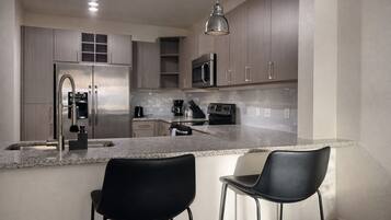 A modern kitchen with stainless steel appliances, a granite countertop, and two black bar stools.