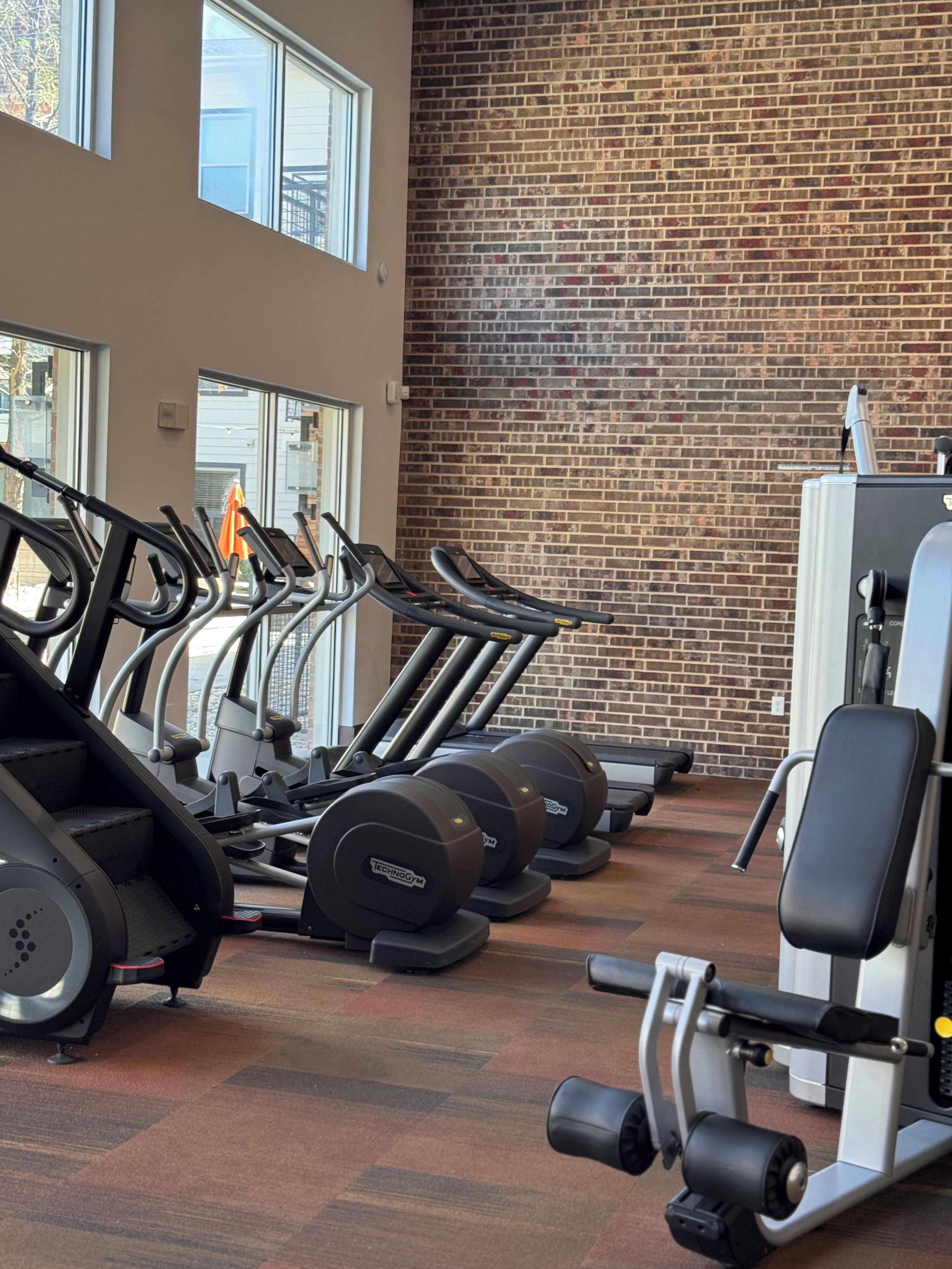 Un gimnasio con cintas de correr, máquinas de pesas y una pared de ladrillo.