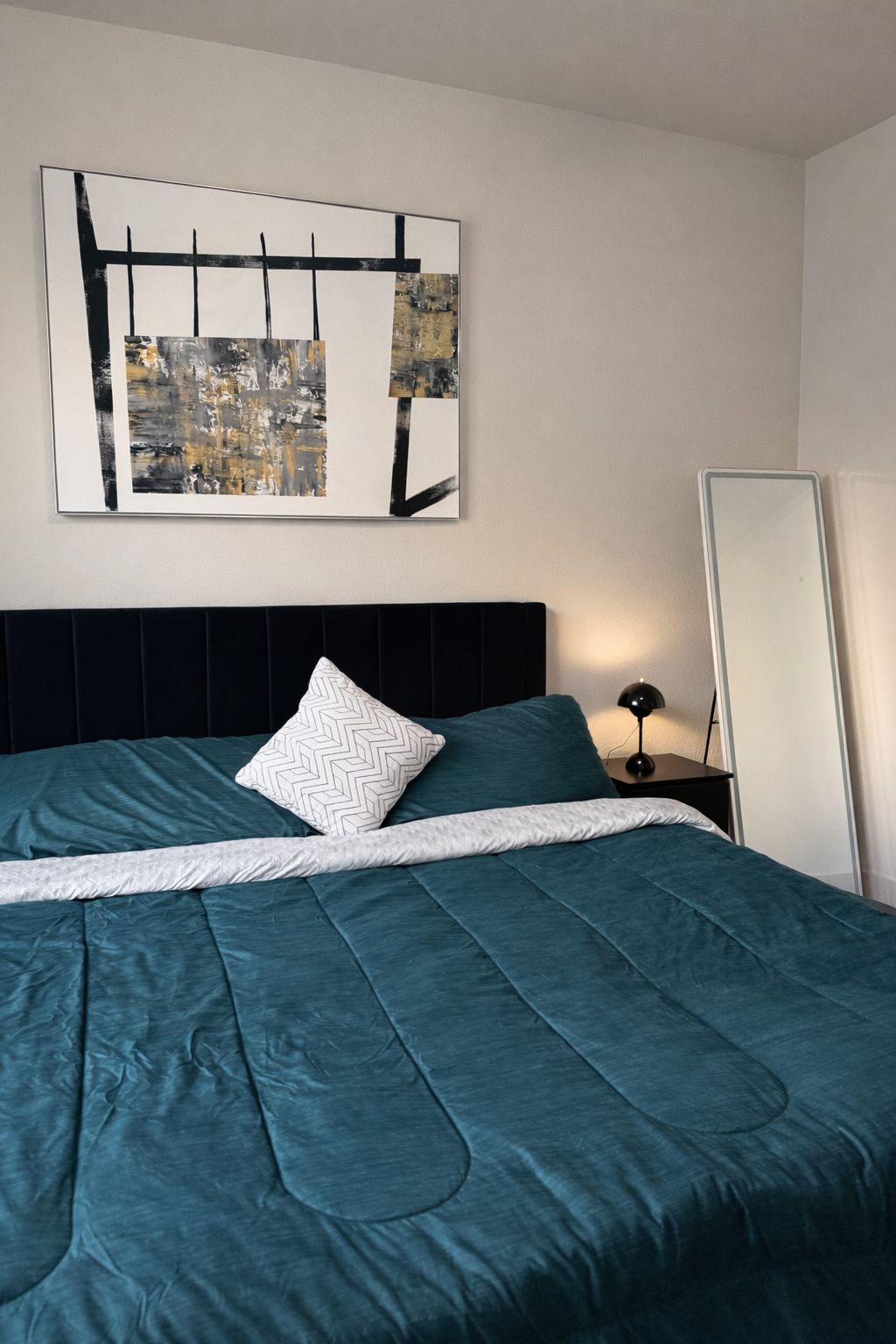 A neatly made bed with a teal bedspread and a white pillow with a chevron pattern.